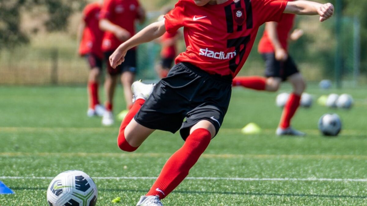 En fotbollsspelare klädd i rödsvarta kläder är just i färd med att sparka bollen.